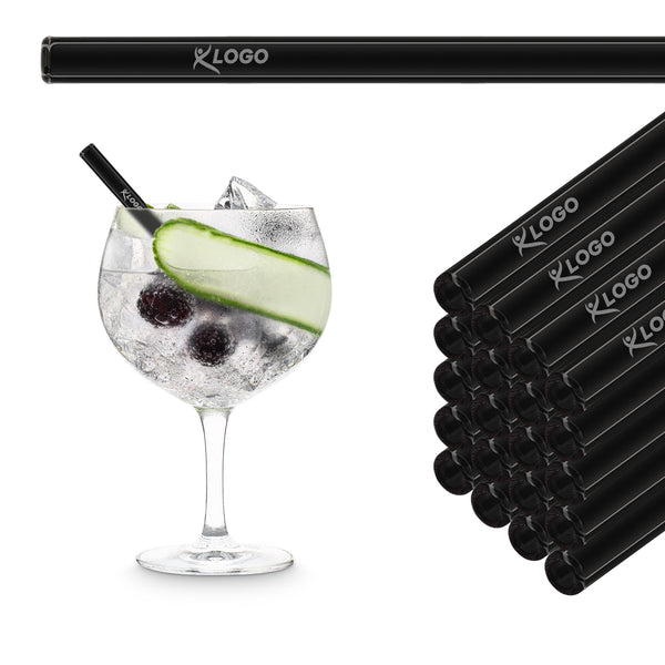 Black 15 cm HALM glass straws with sample logo engraving stacked beside a gin and tonic with cucumber in a balloon glass
