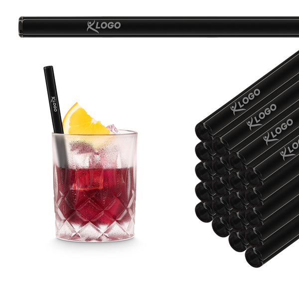 Schwarze 15 cm HALM Glasstrohhalme mit Beispiel-Logogravur im Stapel neben einem roten Cocktail im Tumbler
