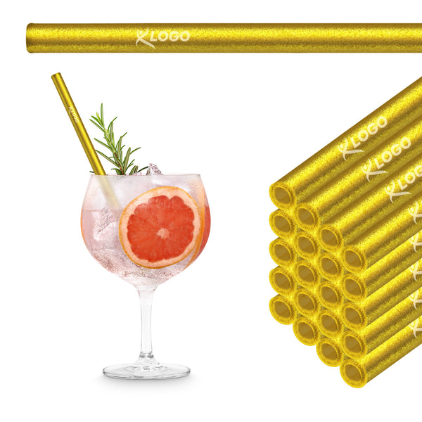 Goldene 20 cm HALM Glasstrohhalme mit Beispiel-Logogravur im Stapel neben einem Grapefruit Gin Tonic im Ballonglas